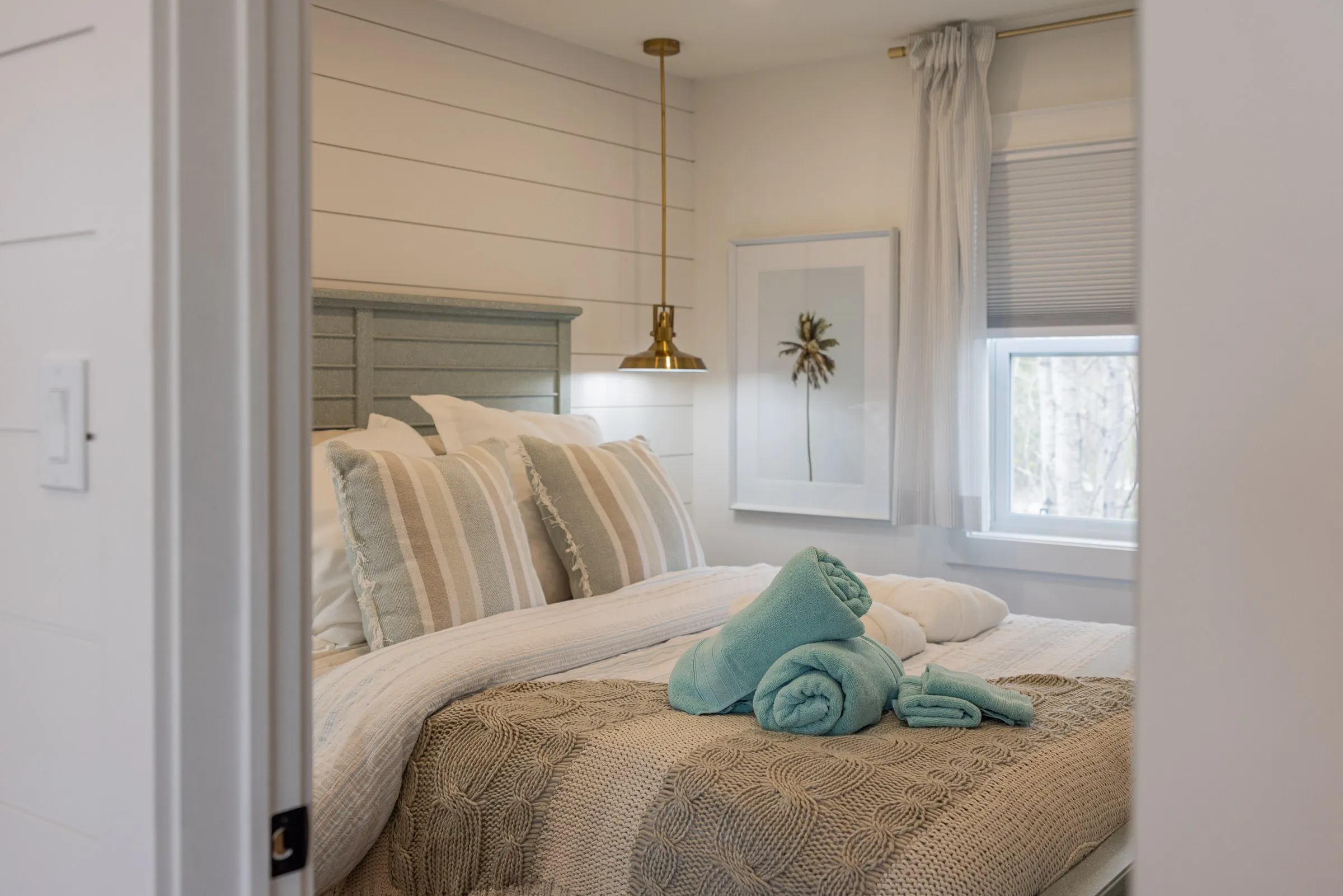 The Beach bedroom seen through the doorway, with a sage headboard and bedside pendant light.
