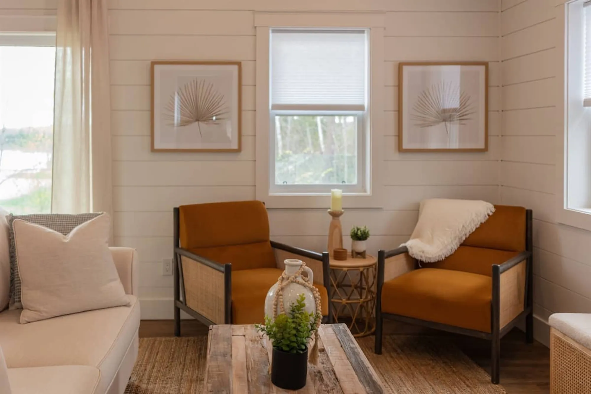 The Beach sitting area, with two rust-coloured cane armchairs, a cream sofa and a reclaimed-wood coffee table under a pair of framed palm-frond prints.