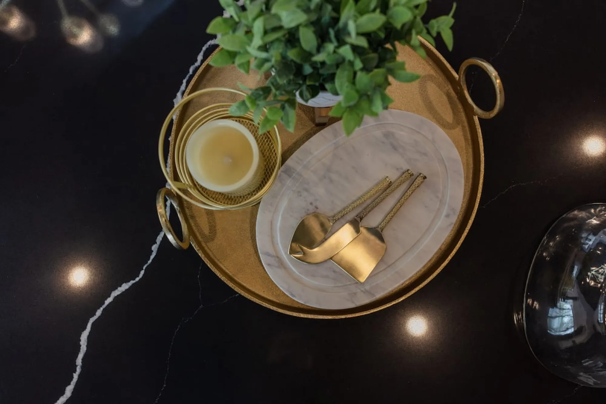 A gold tray on the black marble counter in The Vintage Hollywood, holding a candle, a marble board and brass serving utensils.