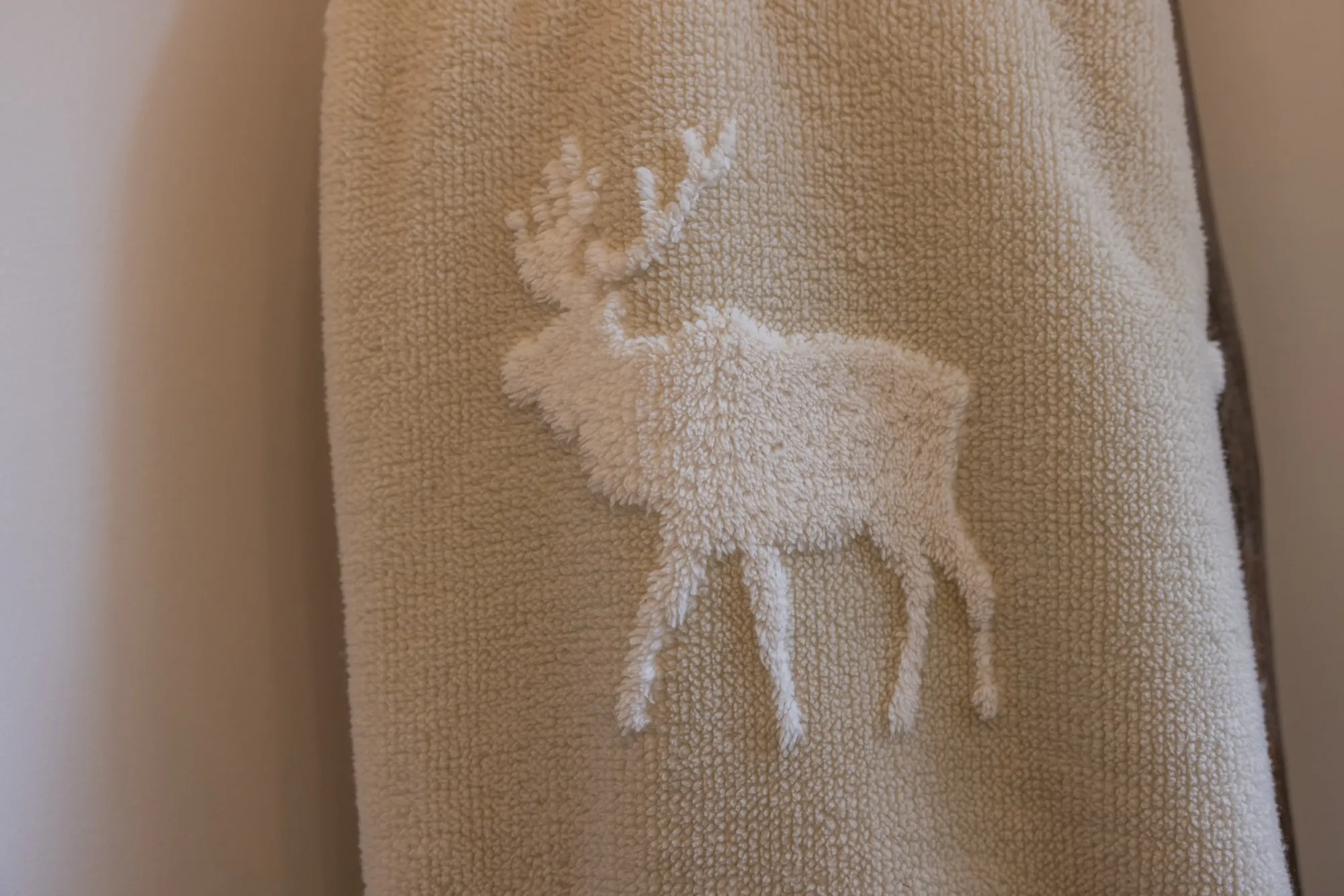 A cream towel with a white embroidered stag motif.