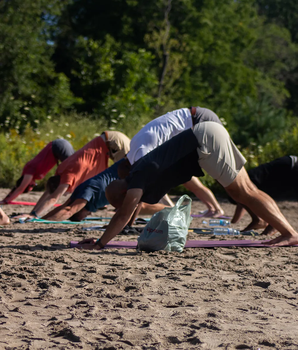 A group practising yoga together on the sandy waterfront.
